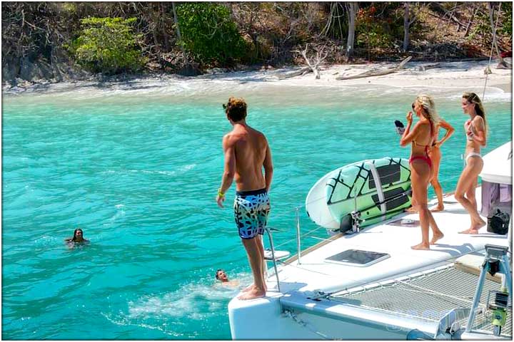 Guy on edge of catamaran in front of secluded beach