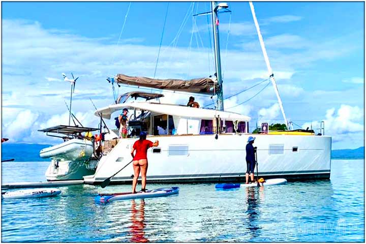 People on stand up paddle boards around sailboat catamaran