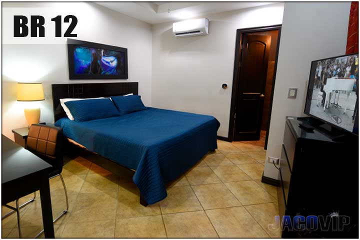 1 king size bed with blue quilted cover, large TV on dresser, and black desk with chair