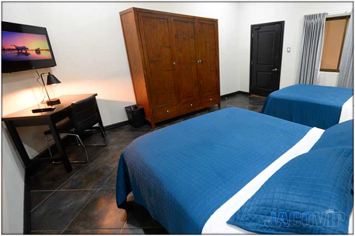 2 queen beds with blue covers, large TV, desk and chair in the corner of the room