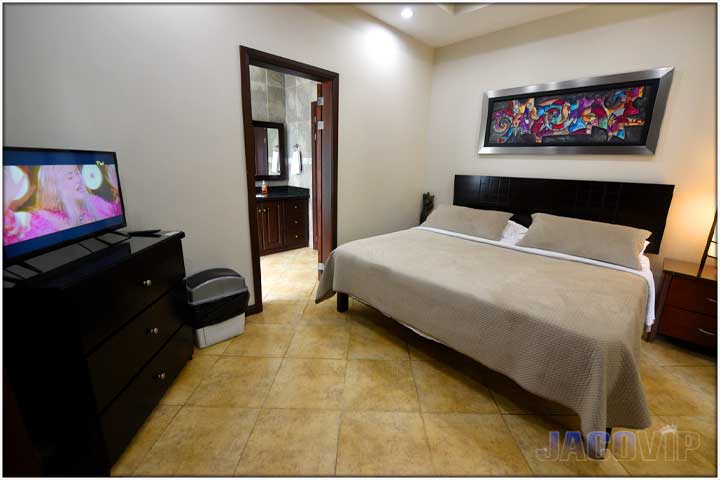 Beige covers and decorative pillows on bed and with TV in the corner