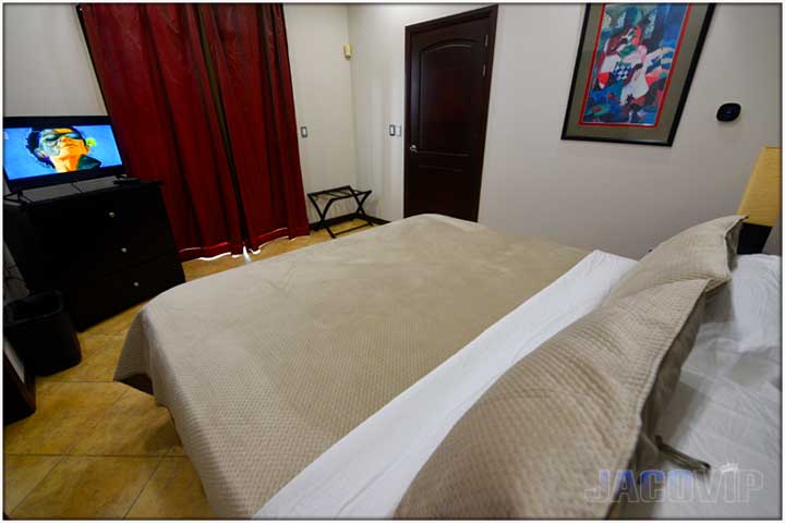 Beige covers and decorative pillows on bed and with TV in the corner