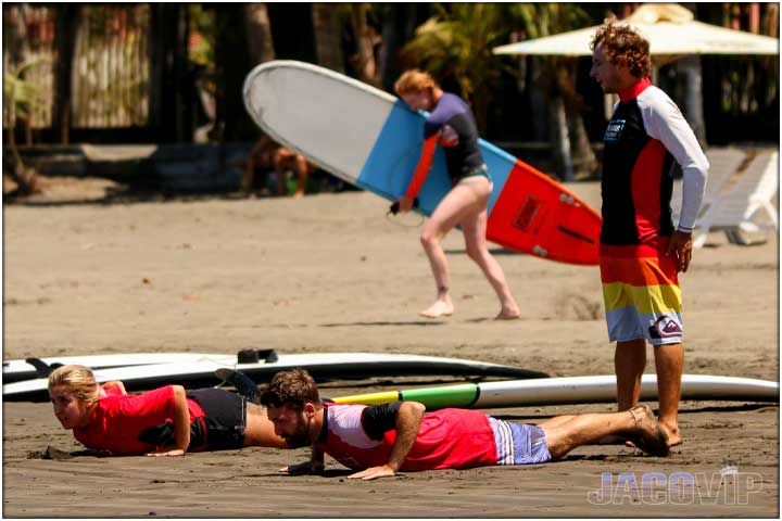 Surf lessons learning to pop up with instructor on beach